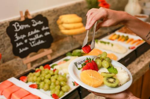 a person holding a plate of fruit with a fork and knife at Ville Hotel Gramadão in Votuporanga