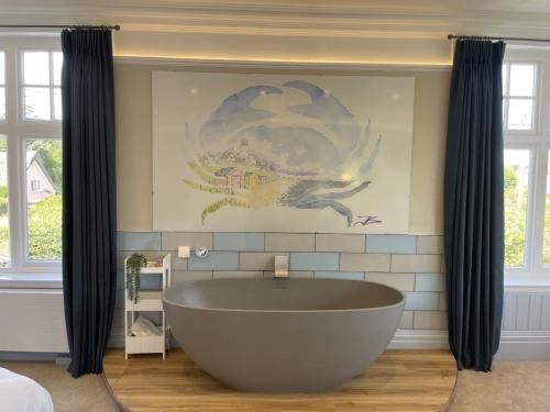 a large tub in a bathroom with a painting on the wall at The Randolph Hotel in Southwold