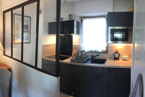 a kitchen with black cabinets and a sink and a window at Domaine privé, , piscine, jacuzzi, joli appartement in Deauville
