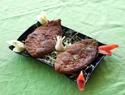 a black plate with two pieces of meat and vegetables at Mango Valley Resort Ganpatipule in Ratnagiri