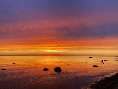a sunset on the beach with rocks in the water at Romantic cozy house Kirzacinas pirts with sauna close to seaside in Skulte