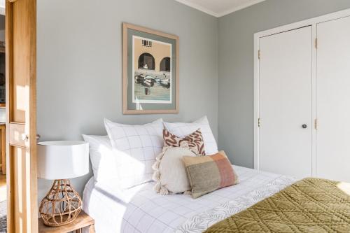 a bedroom with a white bed with pillows on it at Kowhai Cottage & Studio in Raglan