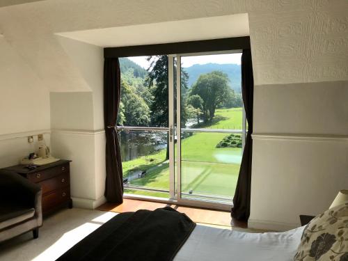 a bedroom with a large window with a view of a golf course at Craig-y-Dderwen Riverside Hotel in Betws-y-coed