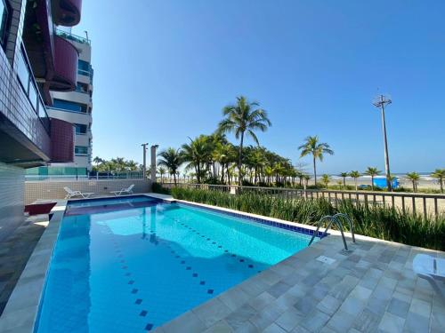 Una piscina con palmeras y un edificio. en APARTAMENTO Pe na Areia com piscina vista mar bairro nobre, en Bertioga
