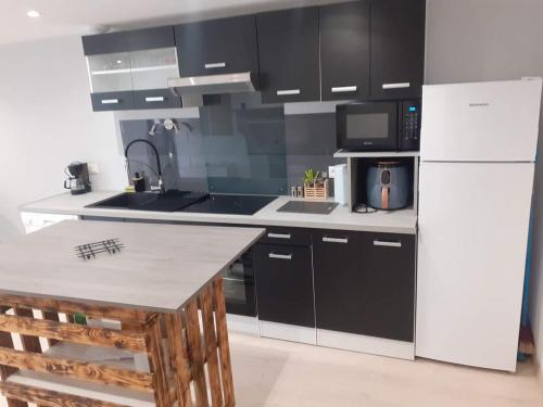 a kitchen with black cabinets and a white refrigerator at LE ROCAGERMANOIS - Jolie maison de village in Saint-Germain-le-Rocheux