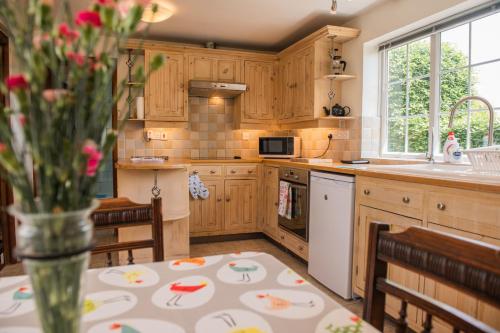 a kitchen with wooden cabinets and a table with a vase of flowers at Farmhouse Cottage at Mollett's Farm in Saxmundham