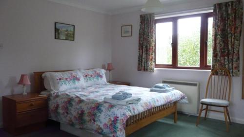 a bedroom with a bed and a chair and a window at Bramley Cottage Holidays in Chichester