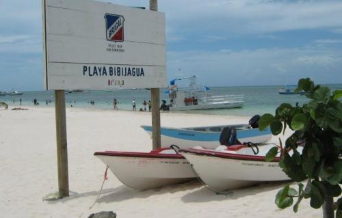 deux bateaux assis sur une plage avec un panneau dans l'établissement L&Y Punta Cana Beach Apartament, à Punta Cana