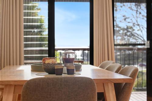 a wooden table with two glasses of wine and a bowl of food at Sun Kissed - As close as you get to Pambula Beach in Pambula Beach