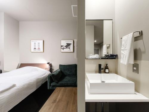 ein Bad mit einem weißen Waschbecken und einem Bett in der Unterkunft Tabist fami THE GREEN OTARU in Otaru