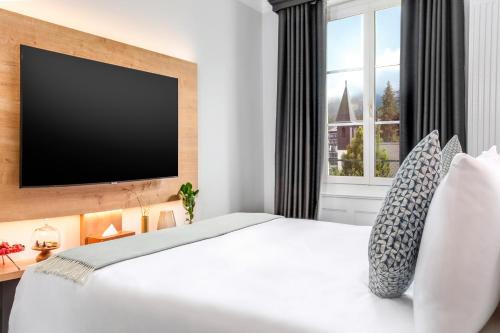 a bedroom with a white bed with a flat screen tv at Villars Palace in Villars-sur-Ollon