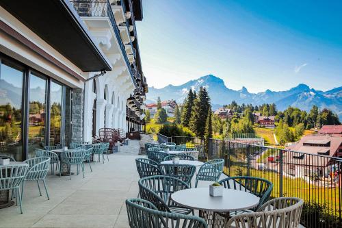 a patio with tables and chairs on a balcony with mountains at Villars Palace in Villars-sur-Ollon