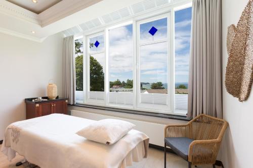 a bedroom with a bed and a chair and windows at Vju Hotel Rügen in Göhren