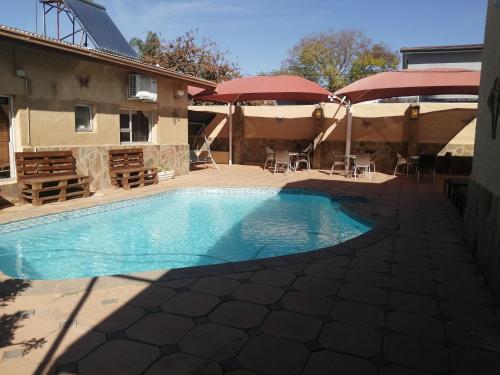 a swimming pool with tables and umbrellas next to a building at Esperanca Guesthouse in Windhoek