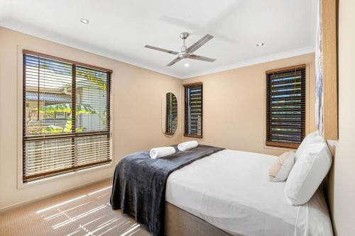 a bedroom with a bed with a ceiling fan and windows at Mudjimba Escape-pet friendly, luxury villa w/ pool in Mudjimba