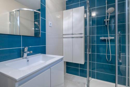 baño con lavabo y ducha con azulejos azules en Maison 6 personnes avec accès privé à la plage !, en Penvins
