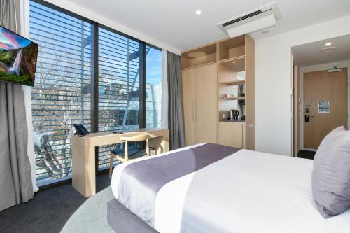 a bedroom with a bed and a desk and a large window at Christchurch City Hotel in Christchurch