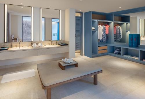 a bathroom with two sinks and a bench and two mirrors at Raffles Maldives Meradhoo in Gaafu Alifu Atoll
