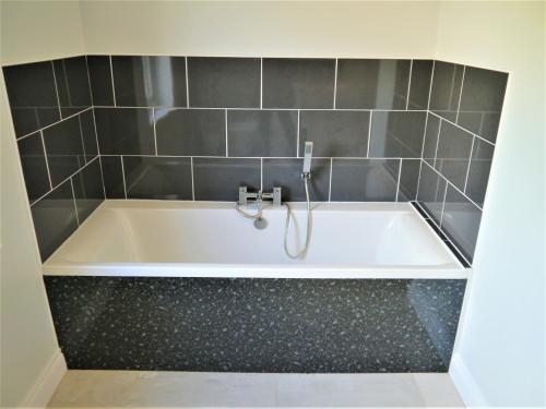 a bath tub in a bathroom with gray tiles at Driftwood in Kippford
