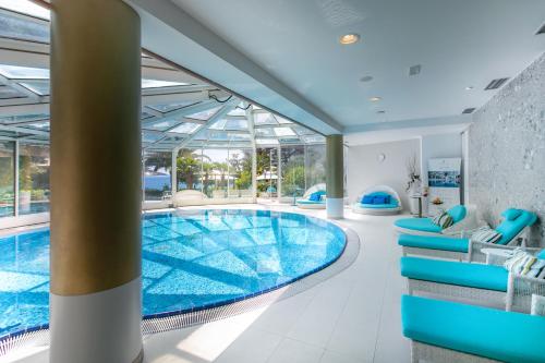 een zwembad in een gebouw met blauwe stoelen en een zwembad bij Amadria Park Hotel Milenij in Opatija