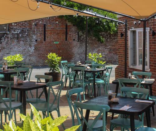 un patio al aire libre con mesas, sillas y una pared de ladrillo en The Kings Head en Whiteparish