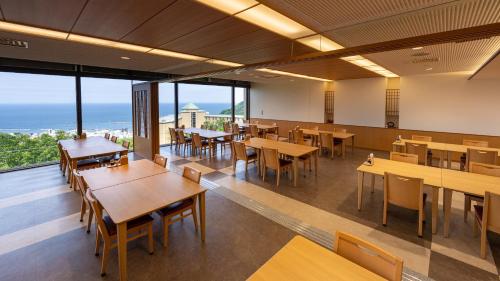 a restaurant with tables and chairs and a view of the ocean at KAMENOI HOTEL Atami Annex in Atami