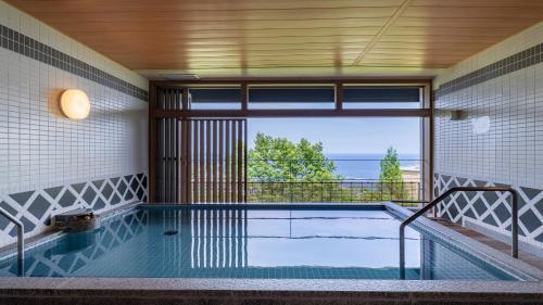 an indoor swimming pool with a view of the ocean at KAMENOI HOTEL Atami Annex in Atami