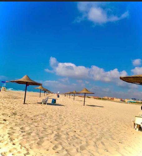 a beach with umbrellas and chairs on the sand at شالية 180م بالروف 180م قرية هليوبيتش الساحل الشمالي للايجار للعائلات فقط in Dawwār ‘Abd al Qādir Qāsim