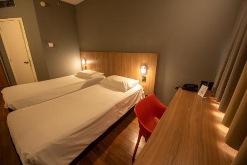 a hotel room with two beds and a red chair at ibis Betim in Betim