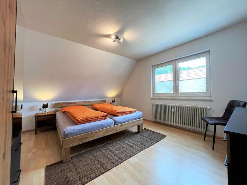 a bedroom with a bed with orange pillows and a window at Ferienwohnung Kinzigblick - Balkon - Für Kinder - mit Bettwäsche & Handtücher in Schenkenzell