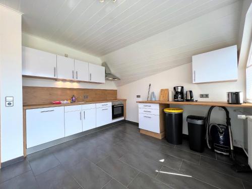 a large kitchen with white cabinets and a tile floor at Ferienwohnung Kinzigblick - Balkon - Für Kinder - mit Bettwäsche & Handtücher in Schenkenzell