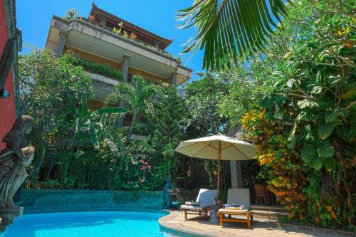 a swimming pool with an umbrella and chairs next to a building at Ellies Hotel in Nusa Dua