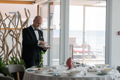 Ein Mann im Anzug, der einen Teller am Tisch hält. in der Unterkunft Grand Hotel Faraglioni in Acitrezza
