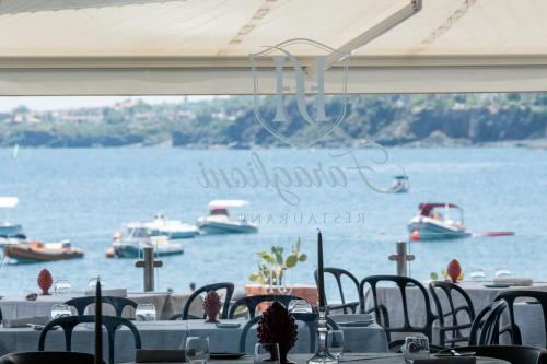 a group of tables and chairs with boats in the water at Grand Hotel Faraglioni in Acitrezza