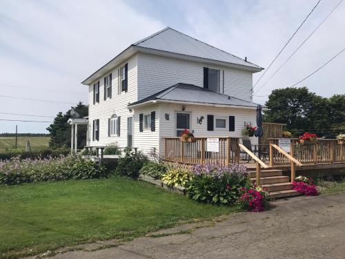 a white house with a porch and some flowers at The Coastal Country House in New Brunswick in Cape Tormentine
