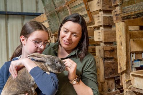 a woman petting a rabbit with a girl at Logements insolites à la ferme - Yourte, Kota ou Pod in Farbus