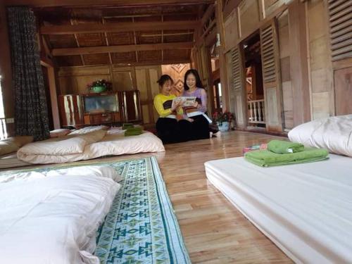 two women are sitting in a room with beds at Thao Ly Homestay Mai Chau in Hòa Bình