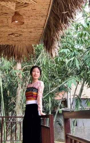a woman standing on a balcony in front of trees at Thao Ly Homestay Mai Chau in Hòa Bình