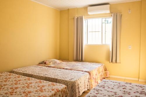 two beds in a yellow room with a window at Casa c lazer à 750m da Barra de Santo Antônio AL in Barra de Santo Antônio