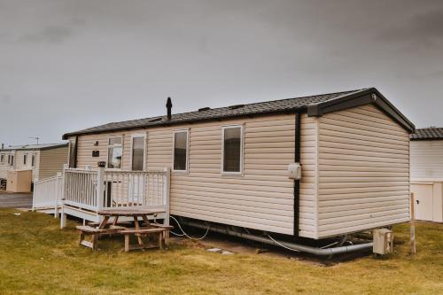un mobile home avec une terrasse couverte et un banc dans l'établissement Cosy Caravan Craig Tara, à Ayr