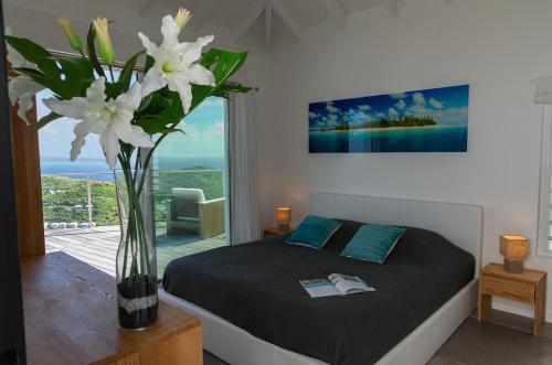 Villa La Vue - Vue panoramique sur les lagons في غوستافي: غرفة نوم مع سرير مع مزهرية مع الزهور البيضاء