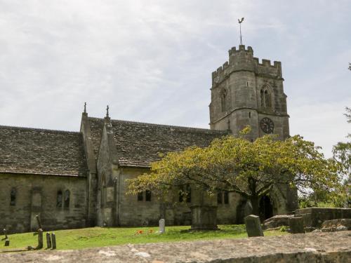 an old church with a tower with a clock on it at Nympy Cottage in Nympsfield