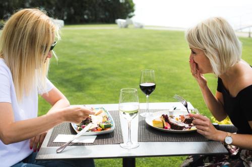 two women sitting at a table with food and wine at Tópart Hotel in Balatonvilágos