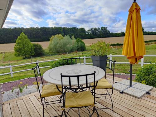 einen Tisch, Stühle und einen Regenschirm auf einer Holzterrasse in der Unterkunft Gîte équestre. Ferme des Essarts in Maucomble