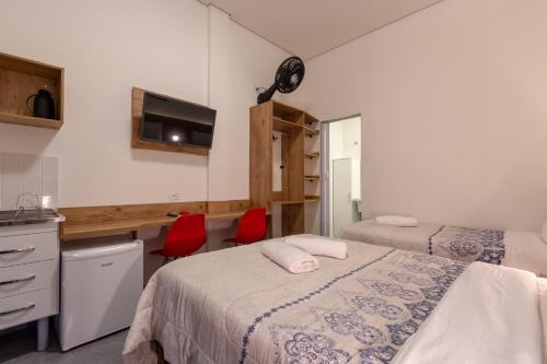 a room with two beds and a desk and two red chairs at BH Studios Hotel Brás in Sao Paulo