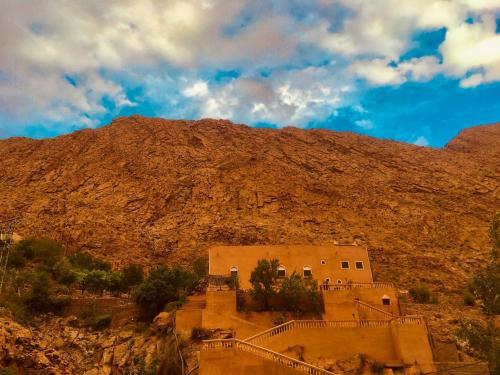 un edificio en una colina con una montaña en el fondo en Hôtel panoramique de la vallée en Aït Idaïr