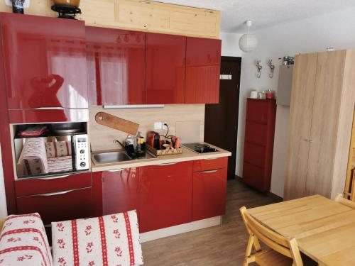 cocina con armarios rojos, fregadero y mesa en Studio les fleury en Mieussy
