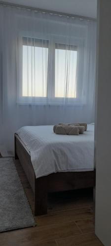 a bed in a white room with two windows at Apartmani Sunlight in Vrnjačka Banja