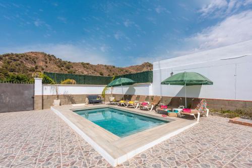 a swimming pool with two green umbrellas and chairs at Villa La marina in Nerja