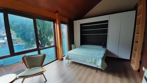 1 dormitorio con 1 cama, 1 silla y ventanas en Monoambiente de diseño único, muy cálido y bien ubicado. 18V2 en San Martín de los Andes